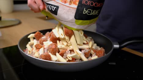 Shot-of-mans-hand-dumping-premade-frozen-pasta-with-sauce-in-it-on-teflon-non-stick-pan-on-the-stove