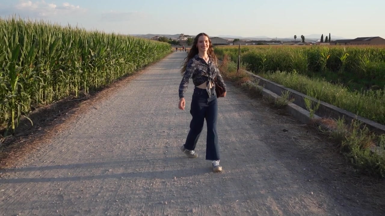Una donna passeggia tranquillamente lungo un sentiero di ghiaia che si snoda attraverso un campo di mais al tramonto.