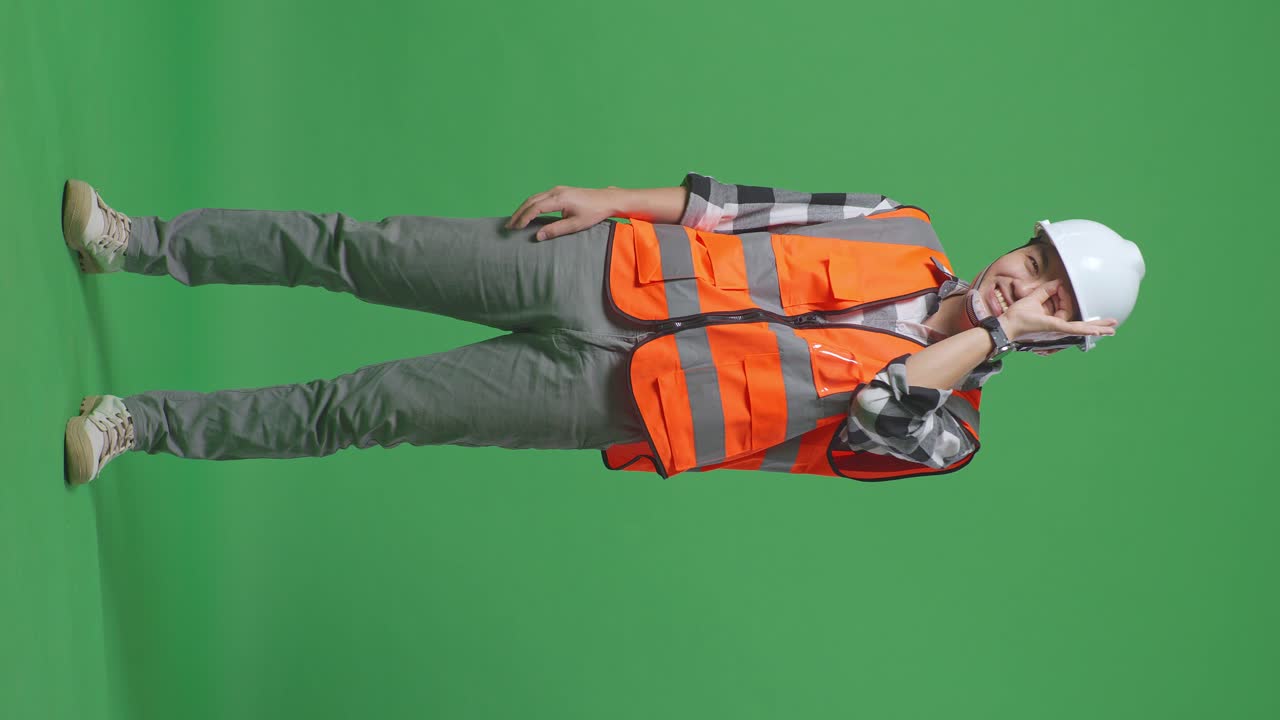 Full Body Of Asian Male Engineer With Safety Helmet Showing Ok Hand Sign Over Eye And Smiling To Camera While Standing In The Green Screen Background Studio