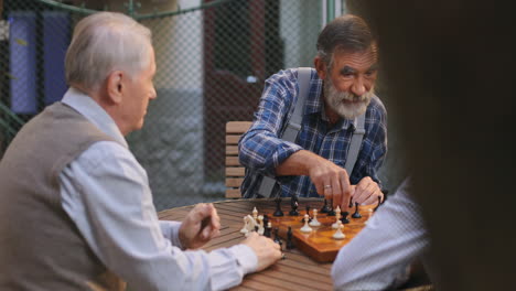 Portrait-Shot-Of-The-Three-Old-Grandfathers-Playing-Chess-Game-In-The-Yard-Outdoors,-One-Man-Moving-His-Figure-And-Others-Feeling-Like-He-Winning