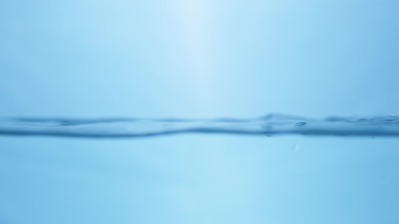 파란색 배경에 물로 가득 찬 용기에 작은 물방울과 파동을 일으키는 물 어리