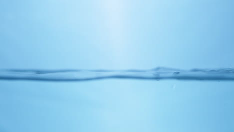 splattering water creating tiny droplets and ripples in a container filled with water against a blue background