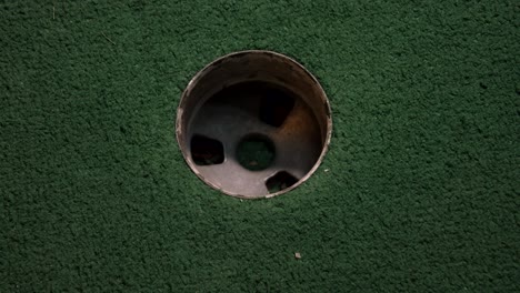 a close up birds eye view of an orange mini golf ball misses the hole on a course