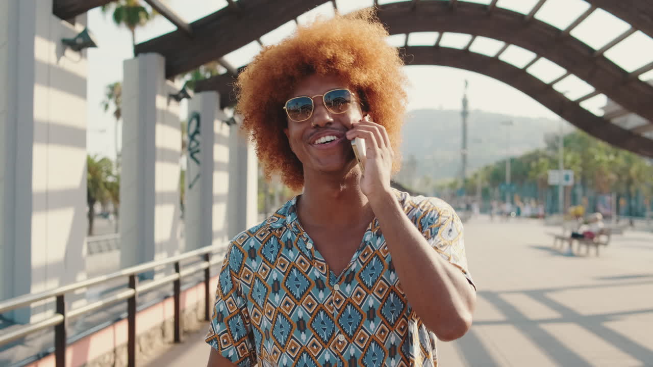 Giovane uomo felice con capelli afro che parla al telefono all'aperto