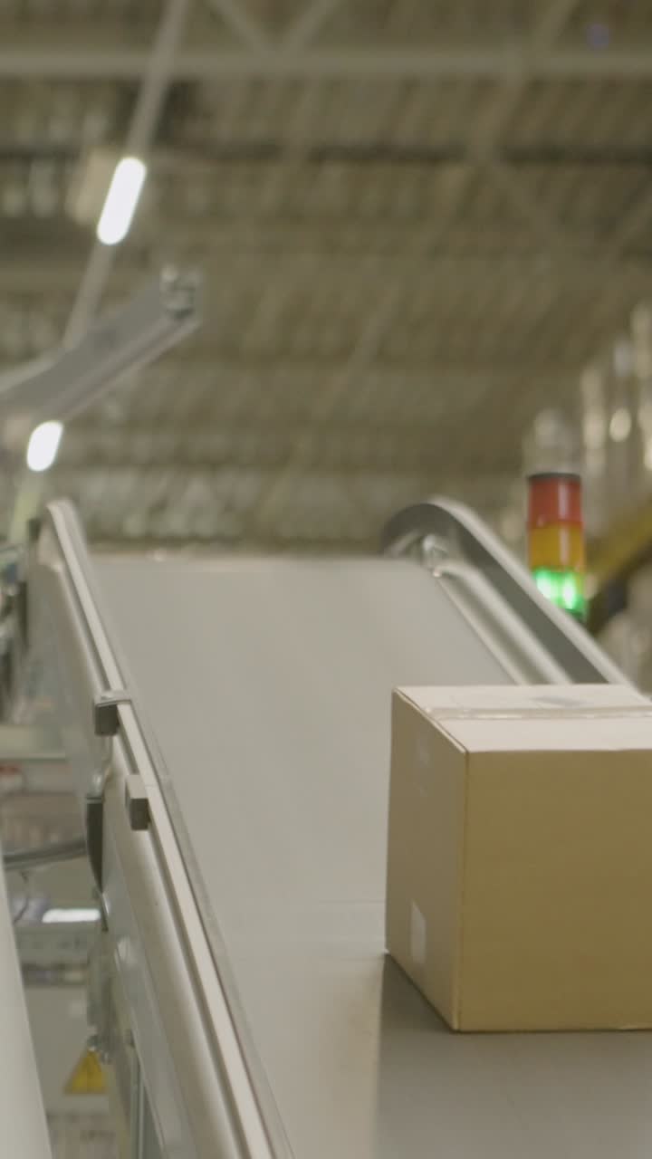 Cardboard box on conveyor belt in busy warehouse, industrial process
