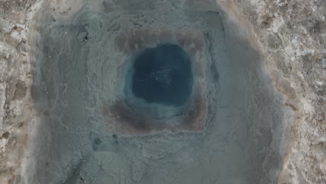 a detailed aerial shot of geysir in iceland during an eruption, showcasing the vibrant blue water and steaming geothermal activity.