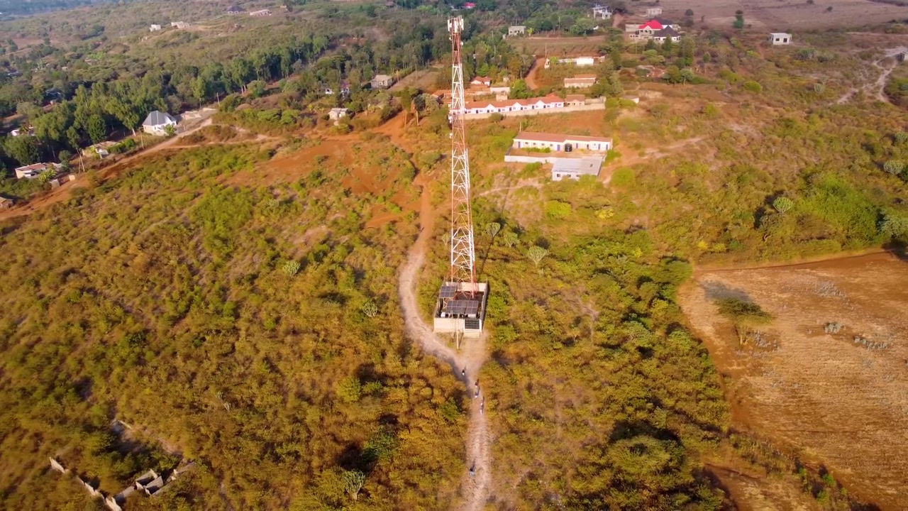 Kenya, Kajiado County, Illasit'te kırsal telekomünikasyon altyapısını ve topluluk gelişimini sergileyen, bir mobil iletişim kulesi üzerinde gezinen drone görüntüsü