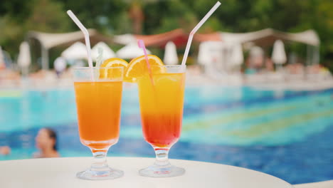 two exotic cocktails on the background of bathing tourists in the pool in a large comfortable hotel