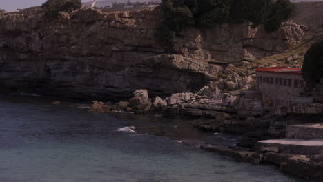 Stone-building-in-historic-harbour-in-Hermanus,-South-Africa-with-cliffs-in-the-background