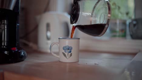 person switch off the electric coffee pot and pour it into a mug