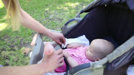 Mother-tending-to-her-baby-girl-in-her-pram-in-the-park