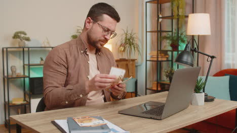 rich happy caucasian man counting money euro cash using laptop calculate domestic bills at home