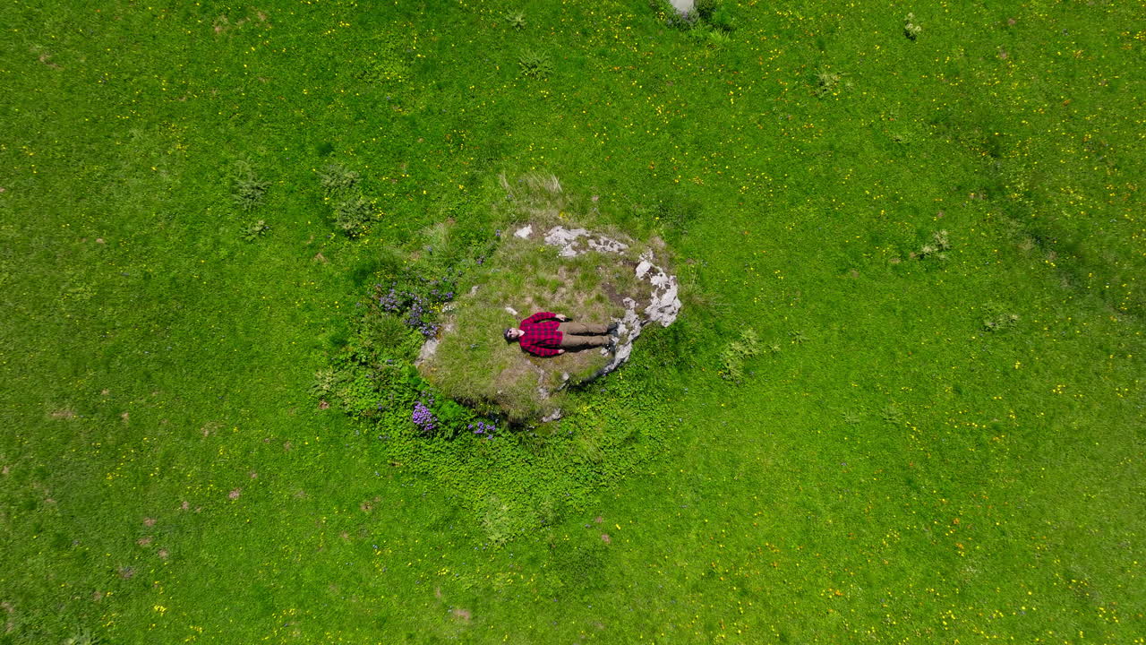 Top down aerial view of a man lying on a green grassy meadow in the Dolomites, Italy