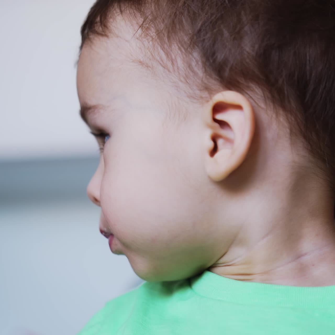 Nice baby boy eating porridge. Kid holds a fork in hand but mom feeds him from spoon. Close up. Blurred backdrop