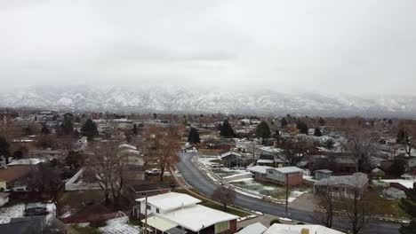 an aerial drone shot tracking backwards over a residential area, in the distance a spectacular view of the wasatch mountains covered in snow on a cold gloomy winter’s day, layton, utah