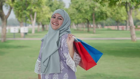 happy muslim woman posing with shopping bags in park