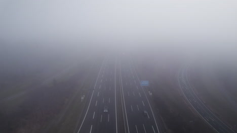 aerial backwards flight through dense clouds above german highway with driving cars on a cloudy day during autumn season