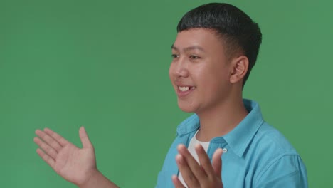 side view of young asian boy blowing kisses to a camera in the green screen studio