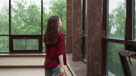 woman looks through terrace window tranquil lady with loose red hair wearing casual clothes enjoys