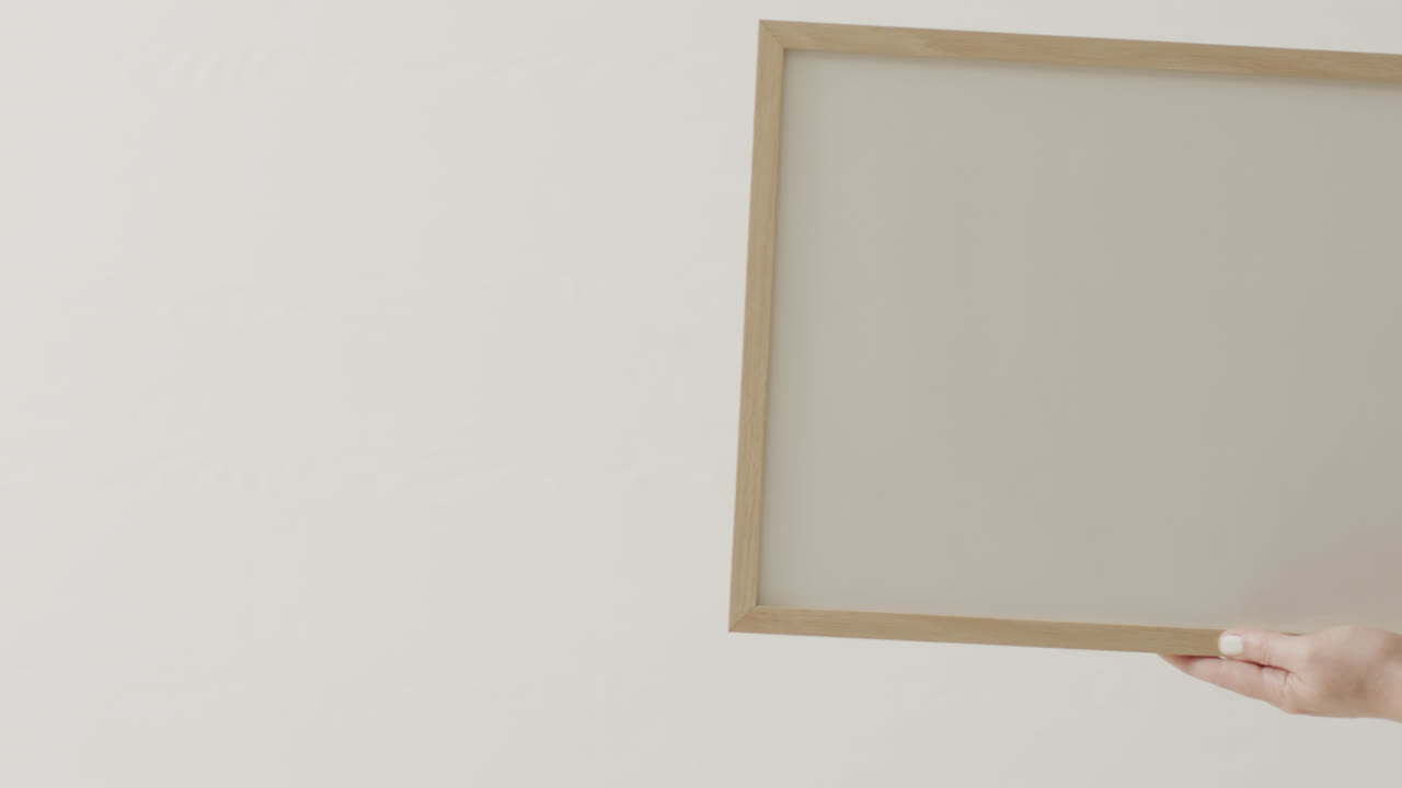 mano de mujer caucásica sosteniendo el marco con espacio de copia en fondo blanco contra la pared blanca