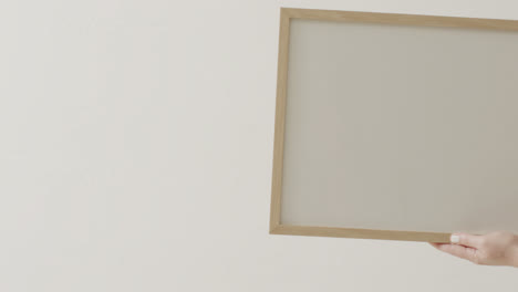 mano de mujer caucásica sosteniendo el marco con espacio de copia en fondo blanco contra la pared blanca