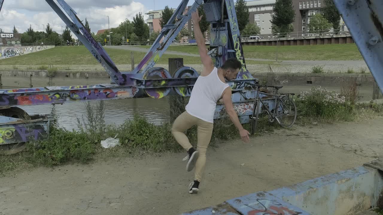 Energetic young male dancer in activewear performing ballet movements and spinning around near shabby metal construction in city