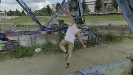 energetic young male dancer in activewear performing ballet movements and spinning around near shabby metal construction in city