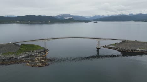 flying over atlantic ocean road in norway with cars passing the lonely bridge on an overcast and cloudy day in summer