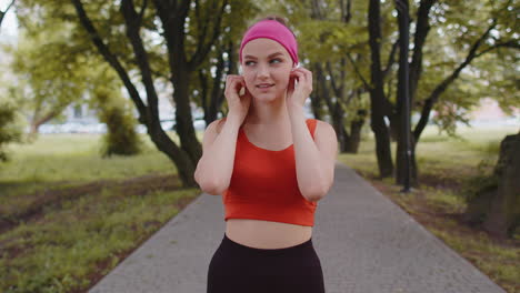 portrait of athletic sport runner girl training, listening favorite music song in earphones in park