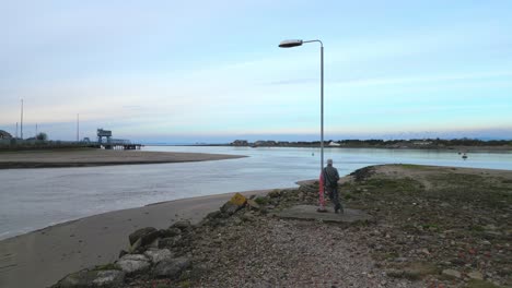 Unusual-solitary-lamppost-with-man-leaning-against-at-the-River-Wyre-estuary-Fleetwood-Lancashire-UK