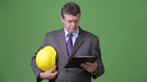 Mature handsome businessman against green background