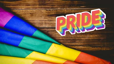 Animation-of-pride-text-and-rainbow-flag-over-wood-table-background