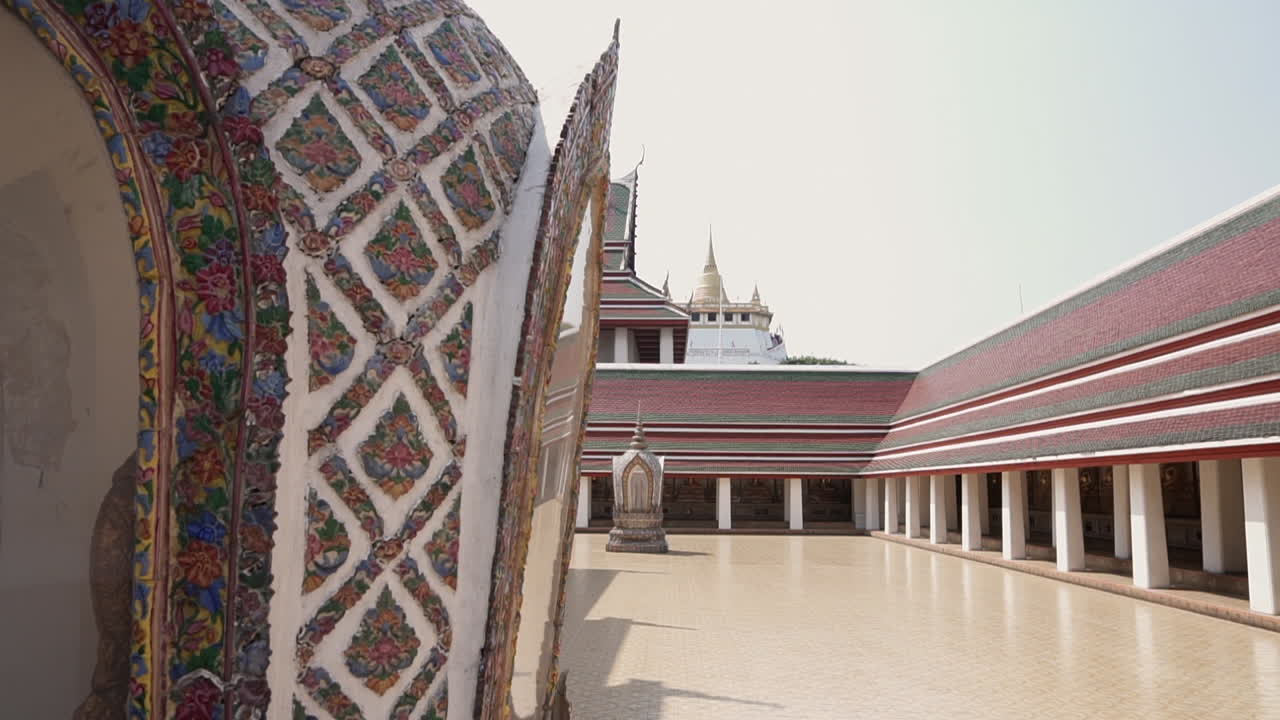 タイ、バンコク市内にある黄金の山仏教寺院を映し出すため、別の人気のない寺院の敷地からカメラを右にスライドまたはパンする。
