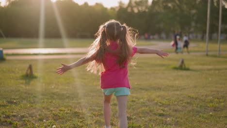 Little-girl-with-waving-ponytails-runs-along-lawn-at-sunset