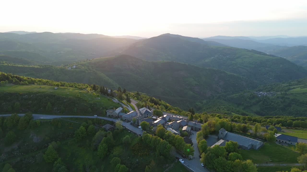 Aerial dolly in over Galician mountains toward the historic village of O Cebreiro. Key landmark on the Camino de Santiago. Majestic scenery with spiritual and cultural atmosphere.