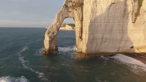 flying trough a natural rock arch of etretat. normandy france, drone view sunset