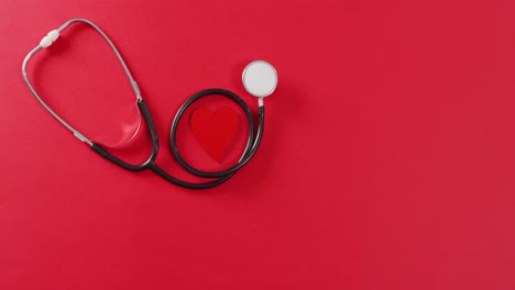 Video-of-close-up-of-heart-and-stethoscope-on-red-background