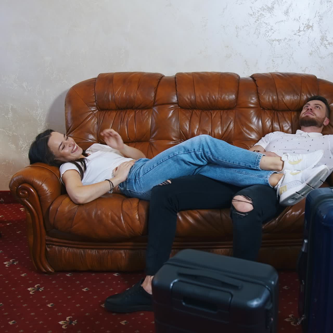 Relaxed man and woman waiting for the departure. Young couple in casual clothes laying on a sofa. Packed suitcases on floor. Finish the vacation