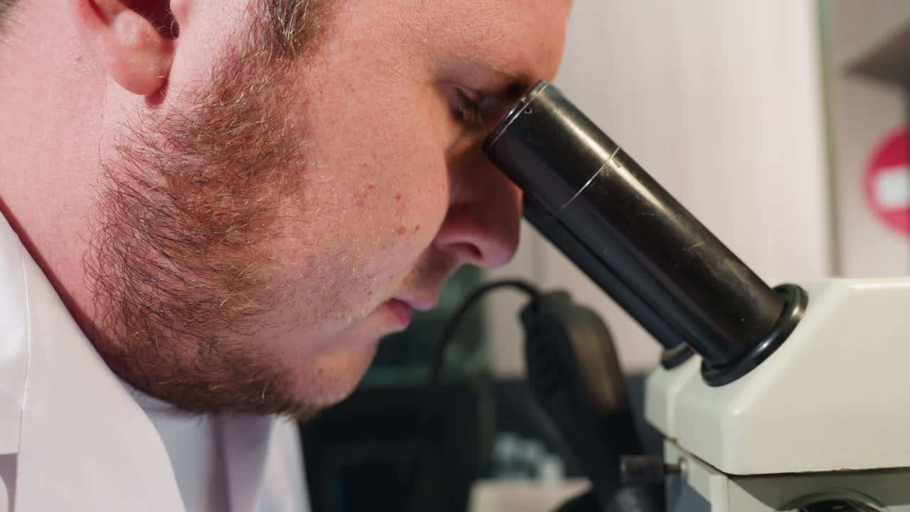 실험실 환경에서 현미경을 사용하는 초점 기술자의 클로즈업 뷰, 그리고 현미경에서 그의 눈을 제거