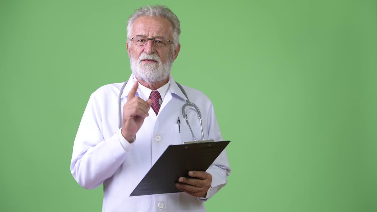 Medico anziano affascinante con la barba su sfondo verde.