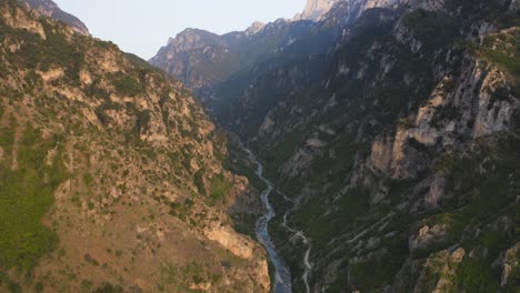 una revisión aérea de drones de un cañón con un río que fluye debajo y picos de montaña en el fondo