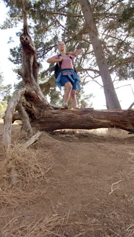 vertical video: hiking in forest, woman with backpack standing on fallen tree trunk