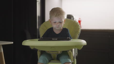 little boy chooses video on tablet and swings legs on chair