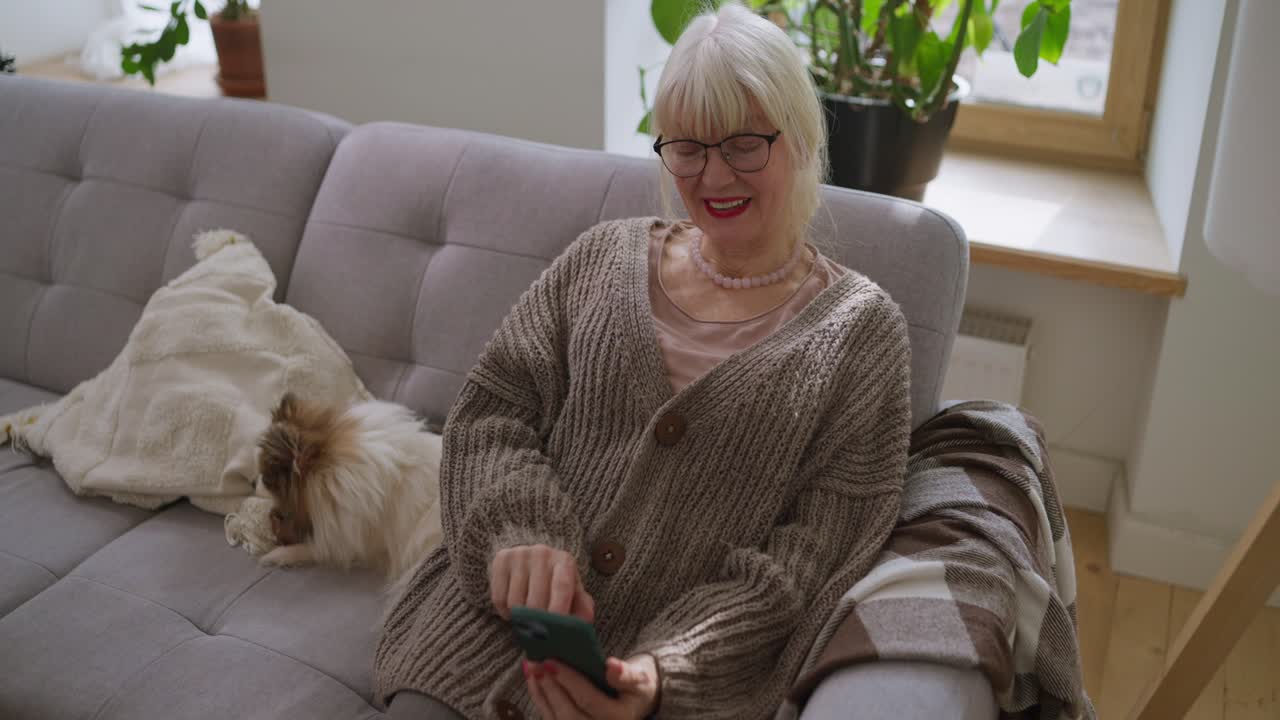 Senior woman with dog using cell phone on couch