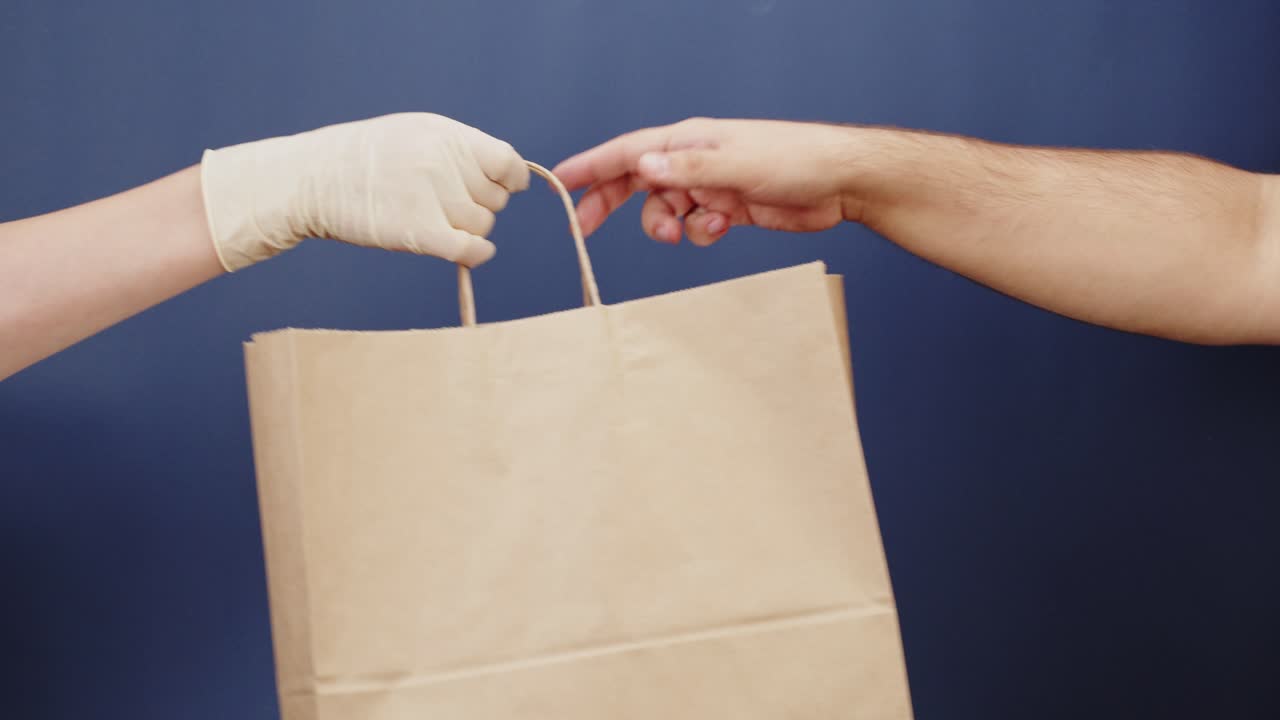 Mano enguantada entregando bolsa de papel a otra mano