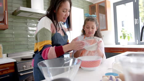 happy biracial mother and daughter preparing dough and smiling in sunny kitchen