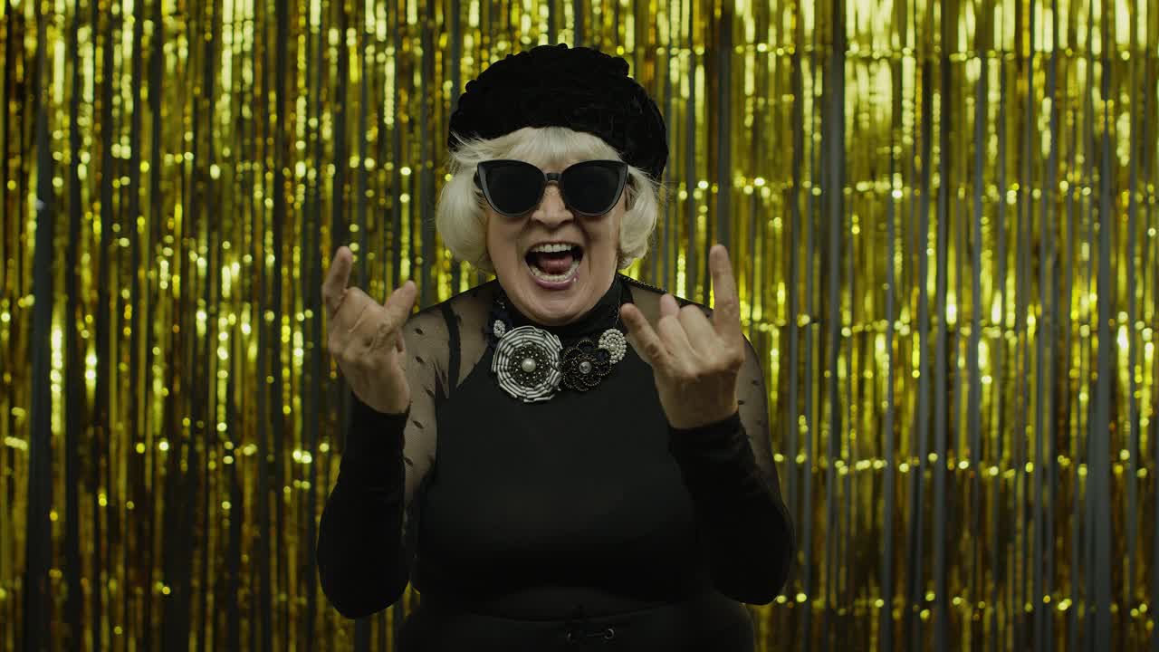 Excited positive senior woman showing rock and roll gesture and sincerely smiling, showing tongue