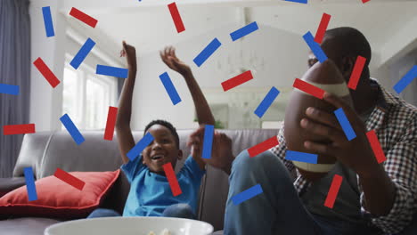 confeti azul y rojo cayendo sobre padre e hijo afroamericanos animando mientras ven deportes en la televisión