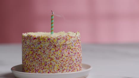 single candle being blown out in studio shot of birthday cake covered with decorations