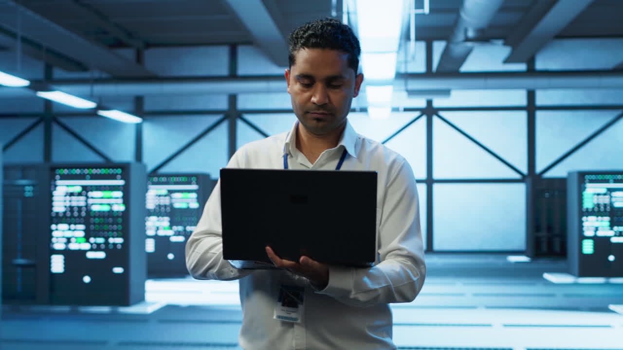 Technician using laptop in data center, managing servers